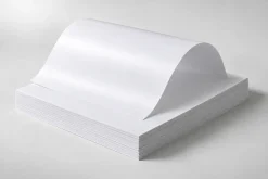 Chồng giấy Couche trắng chưa in với một tờ giấy uốn cong trên bề mặt.