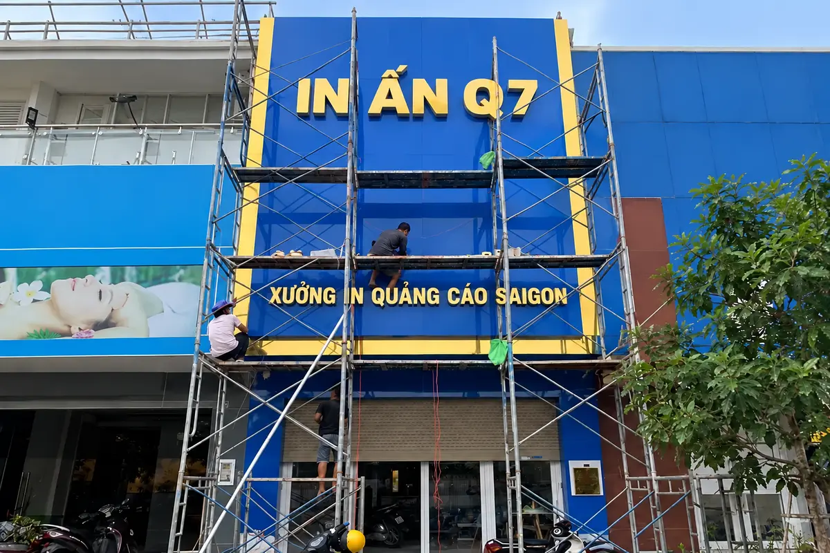 In ấn khai trương – Kỹ thuật viên thi công mặt dựng Alu màu xanh trên hệ giàn giáo tại cửa hàng.