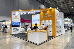 Gian hàng TECH-LONG với bảng hiệu trên cao, vách giới thiệu và quầy tiếp đón trắng vàng.
