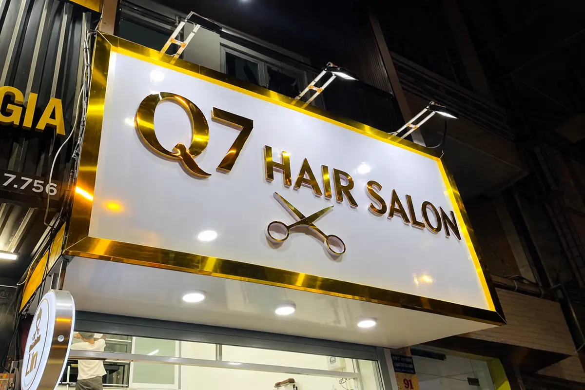 Bảng hiệu salon tóc nền Alu trắng viền vàng, gắn chữ nổi kim loại và đèn rọi.