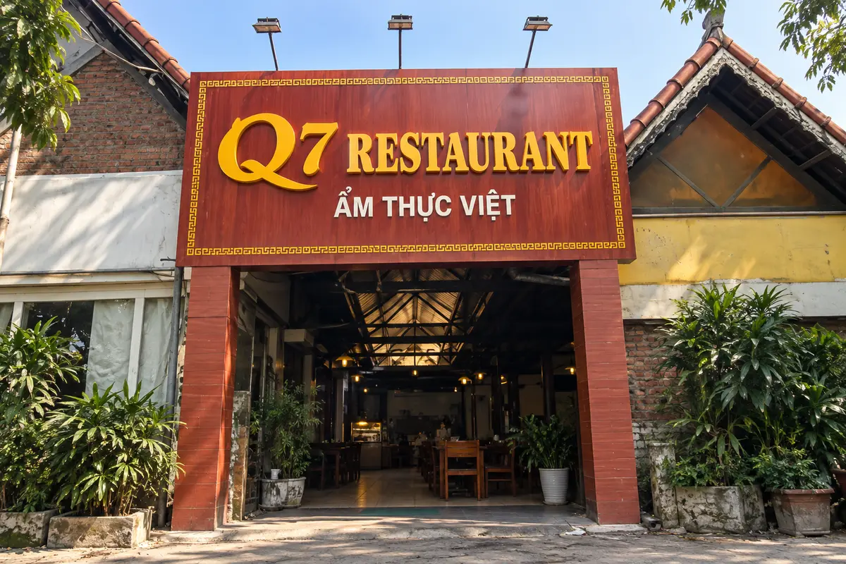 Bảng hiệu nhà hàng nền Alu vân gỗ, gắn chữ nổi màu vàng tại lối vào.