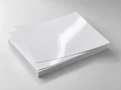 Chồng giấy ảnh trắng chưa in với bề mặt bóng phản chiếu ánh sáng.