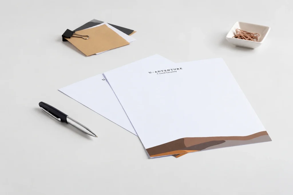 Hai tờ giấy tiêu đề in logo và họa tiết nâu, đặt cạnh bút trên nền sáng.