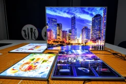 Nhiều khung tranh điện đặt trên bàn, nổi bật là ảnh thành phố phát sáng.