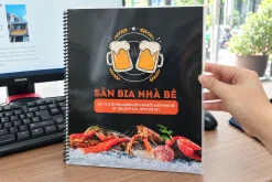 Menu quán bia cầm trên tay, có bề mặt nhựa bóng, viền trong và gáy lò xo.