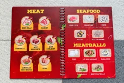 Menu mở hai trang màu đỏ, trình bày các món thịt, hải sản và viên thả lẩu.